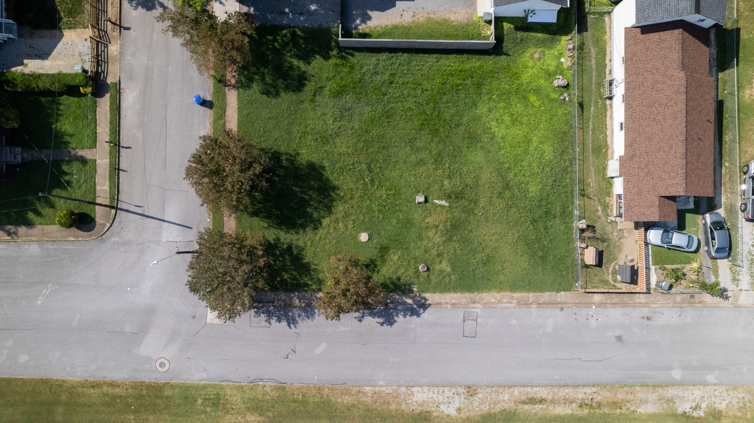 Overhead photo of the vacant grassed corner lot on Beech Street before construction, with neighboring houses and the sidewalk along two frontages
