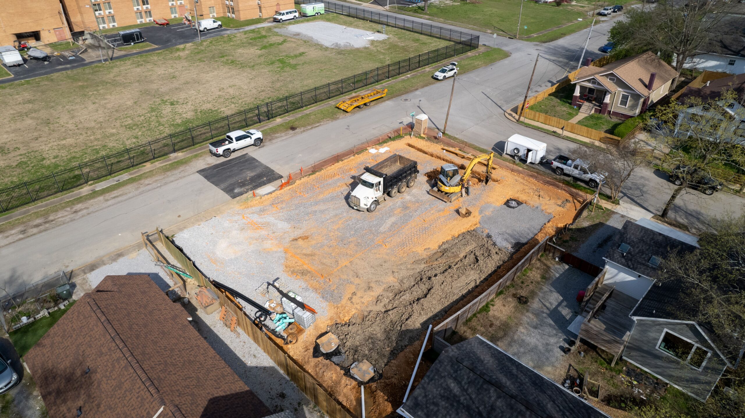 Aerial view of the Beech Street lot during excavation, with a dump truck and excavator working over stone and cut earth inside silt fencing