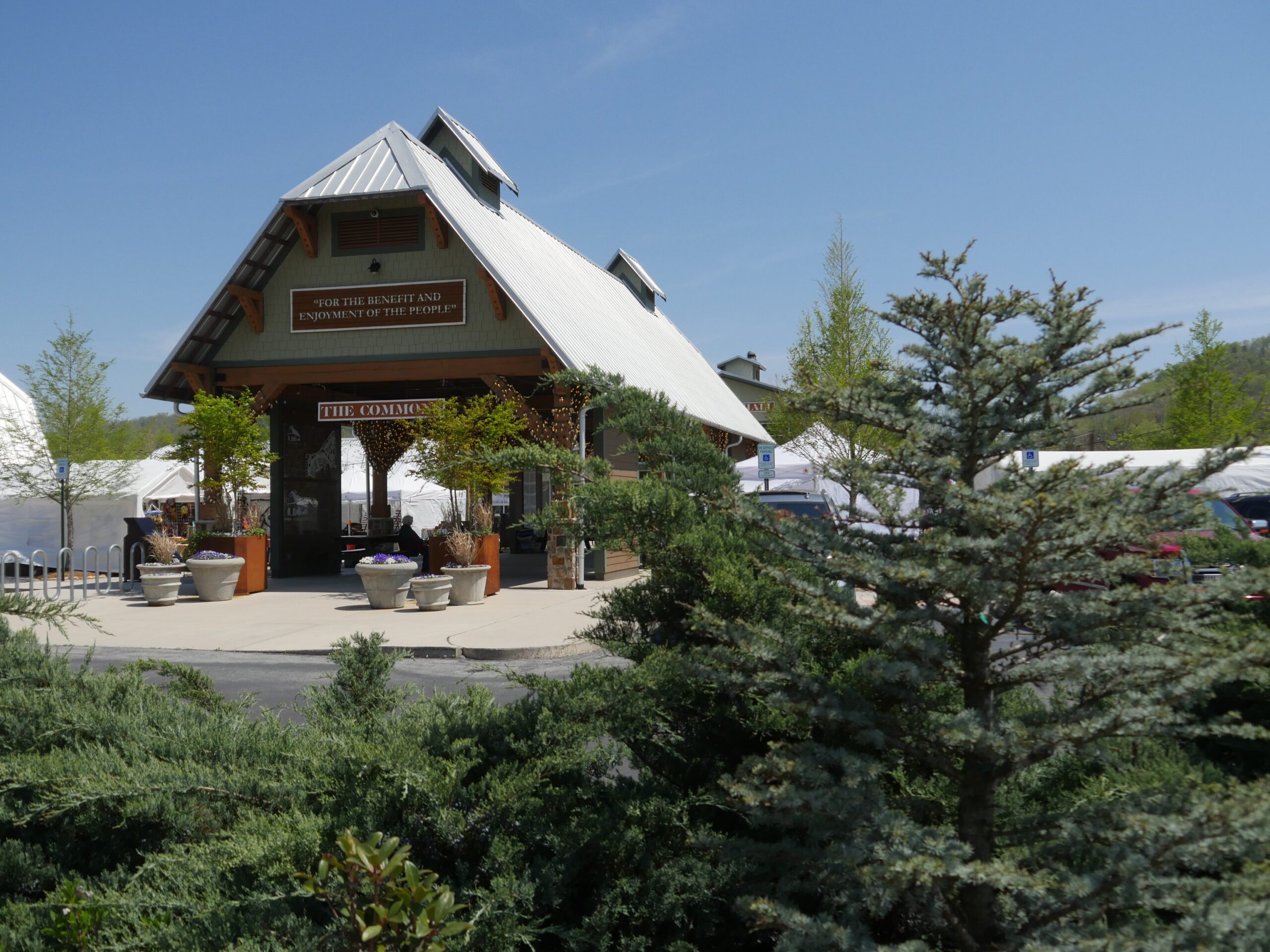 The pavilion and plaza seen across the parking drive through cedar and juniper