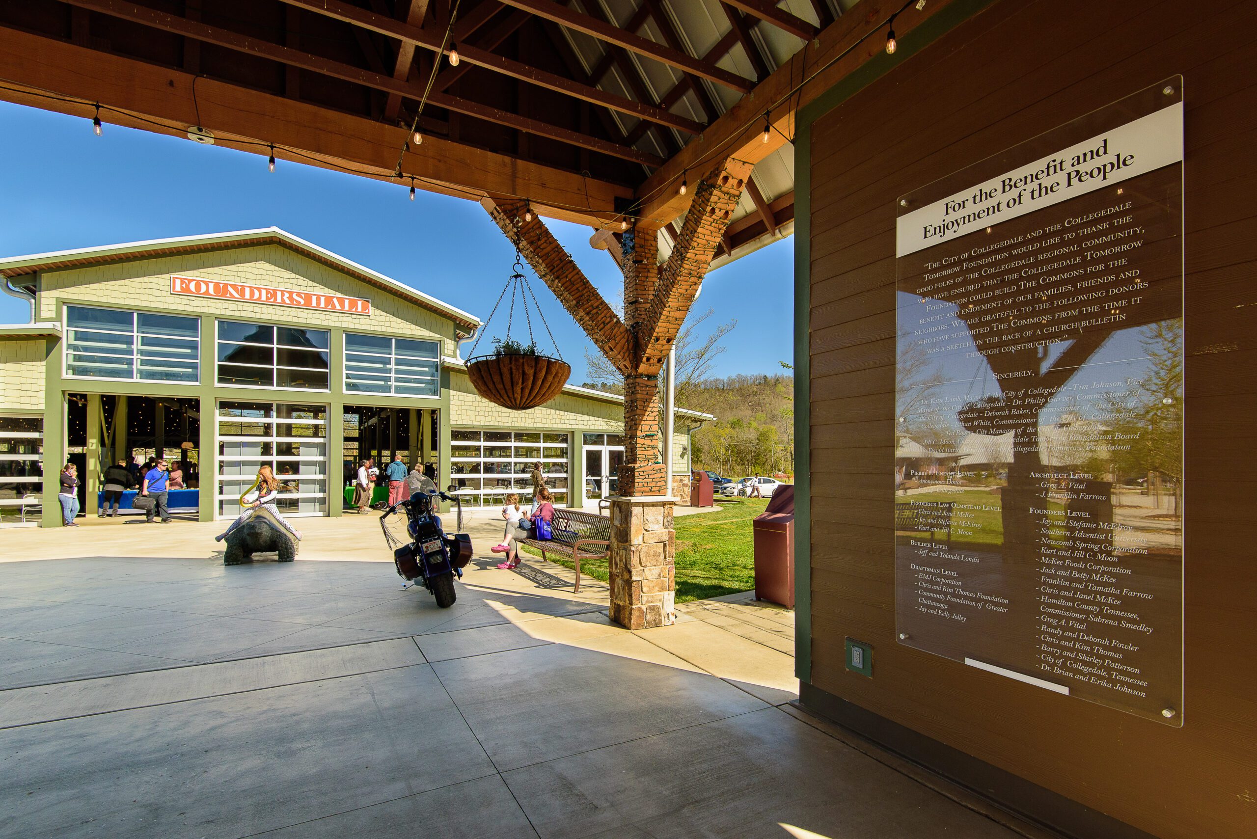 Under the timber pavilion at the Collegedale Commons, with the donor plaque on the wall and Founders Hall across the plaza
