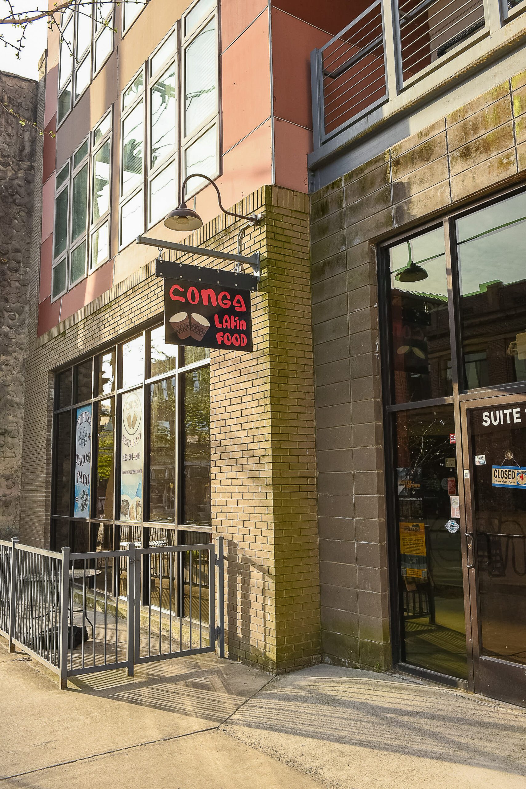 The brick corner of 26 East Main at the restaurant entrance, with a hanging sign and gooseneck light