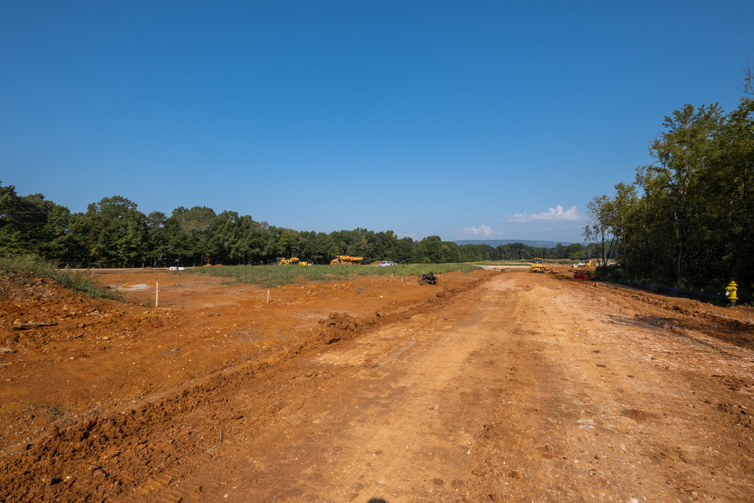 Graded street corridor at The Farmstead with staked lots, a fire hydrant and the ridge line beyond