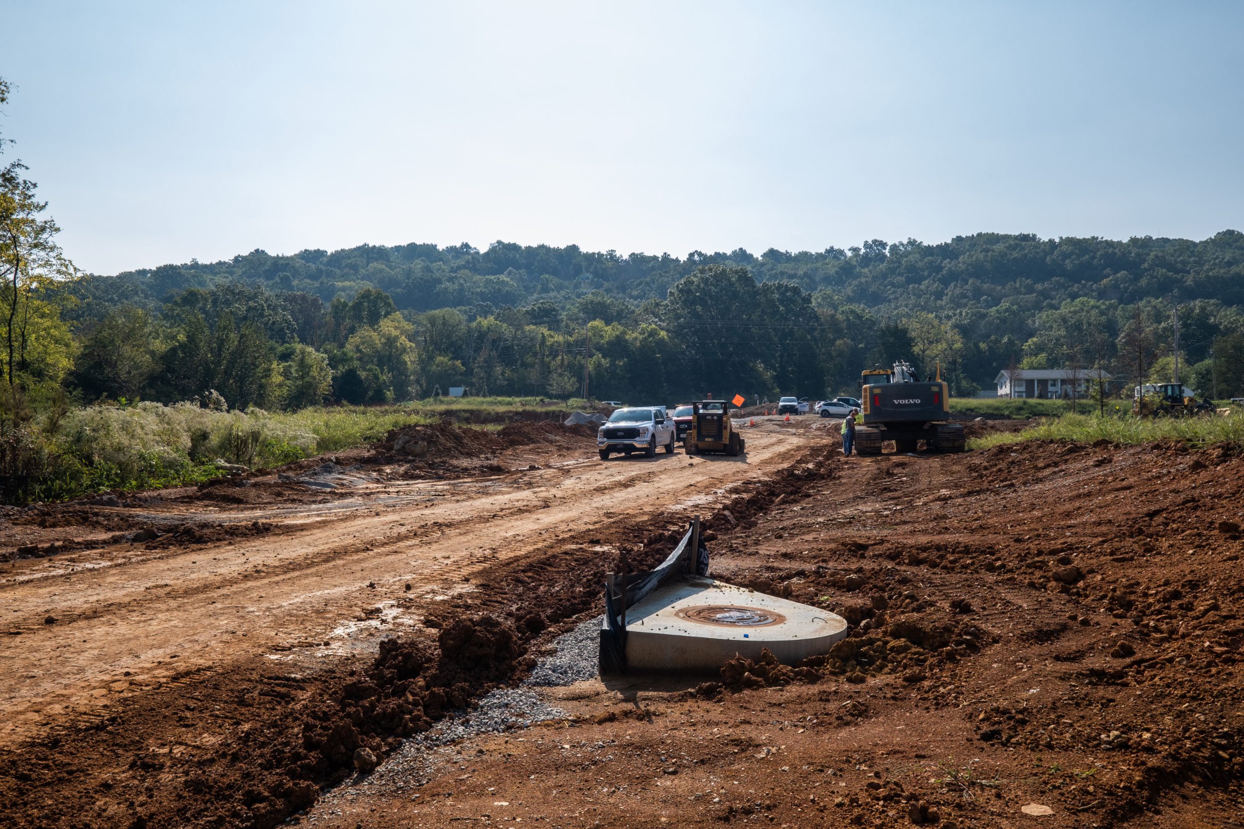 Graded road corridor at The Farmstead with a drainage structure set in place and crews working towards the Hixson tree line
