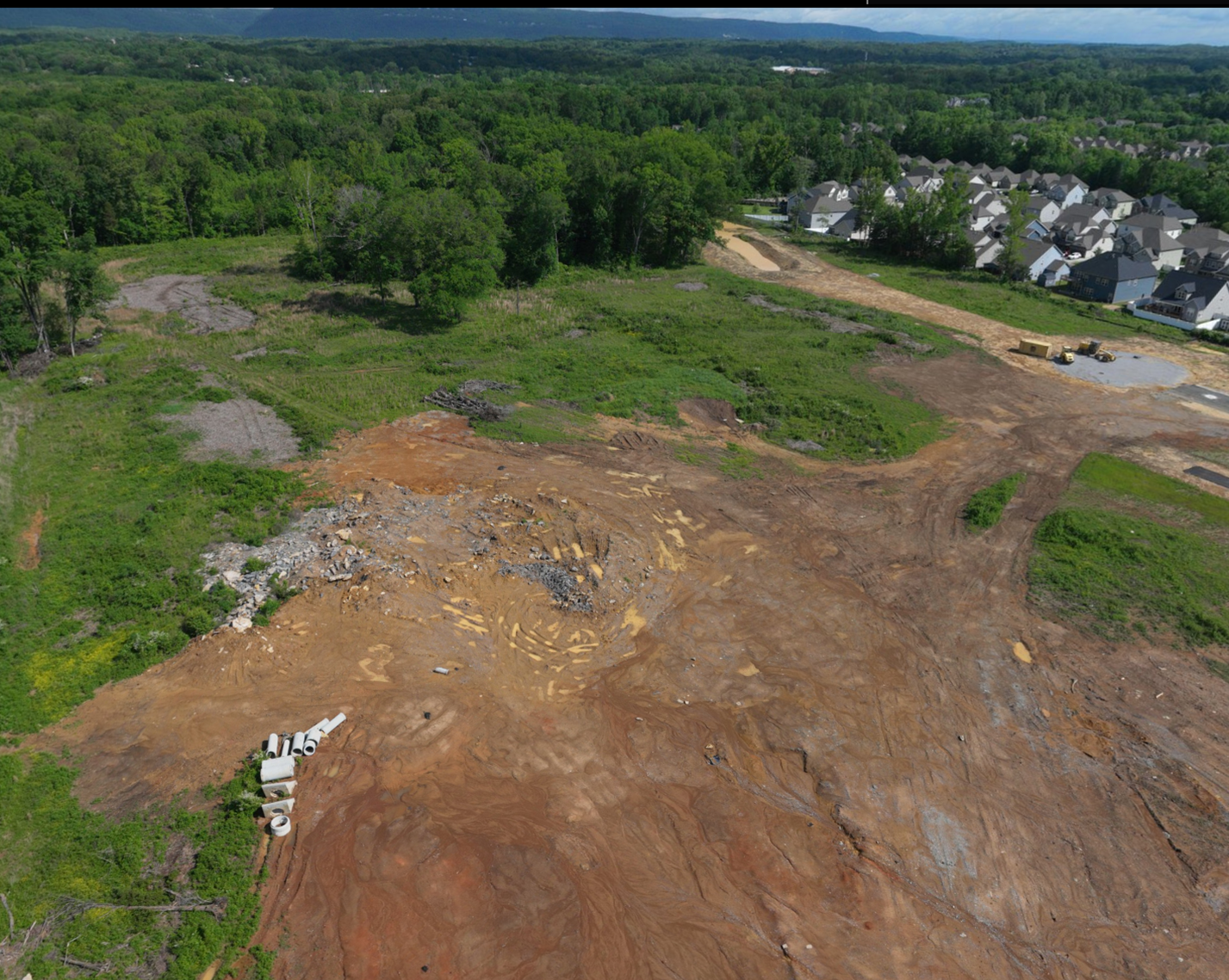 Wide aerial of The Farmstead Phase 2 site with graded ground, stockpiled pipe and the ridge line beyond Hixson