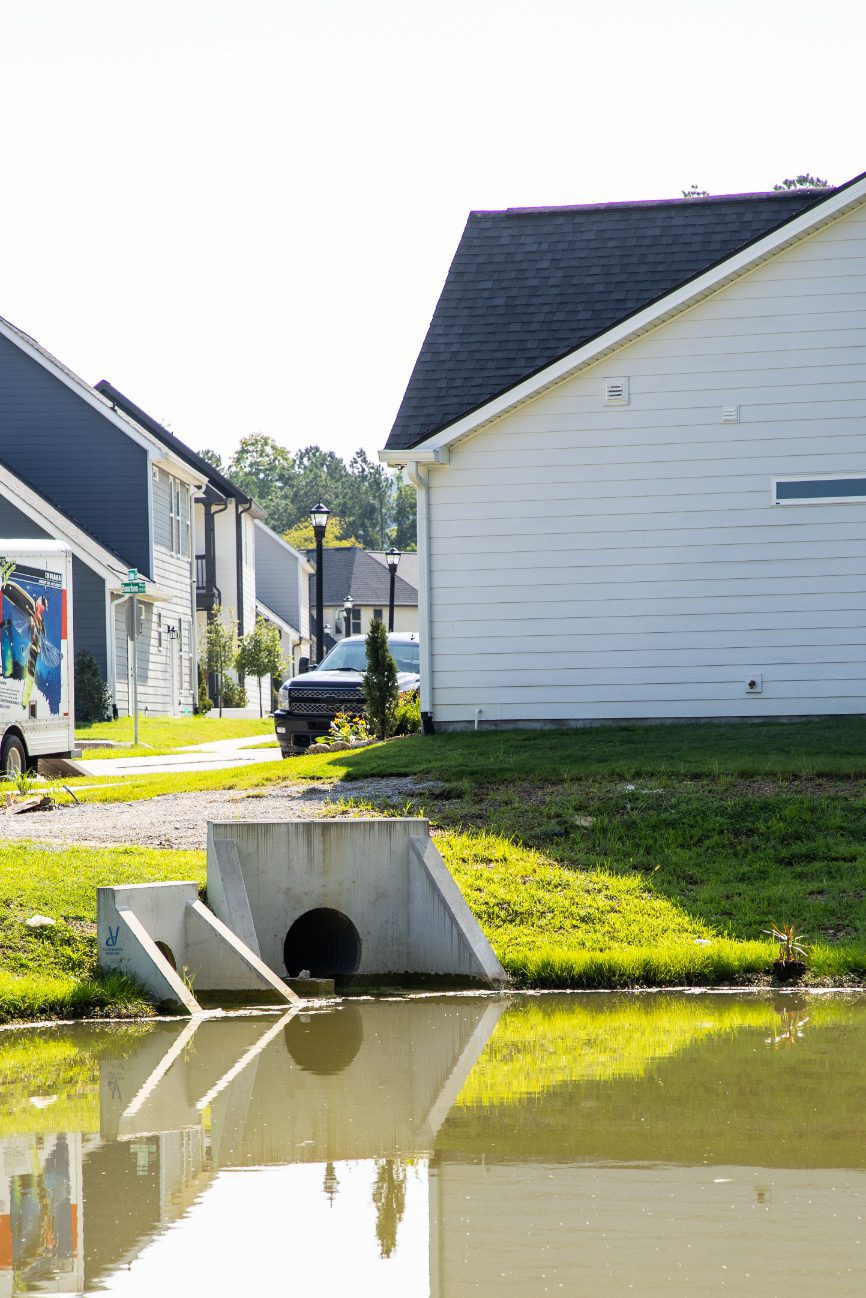 Concrete headwall and outfall pipe beside homes, reflected in the pond
