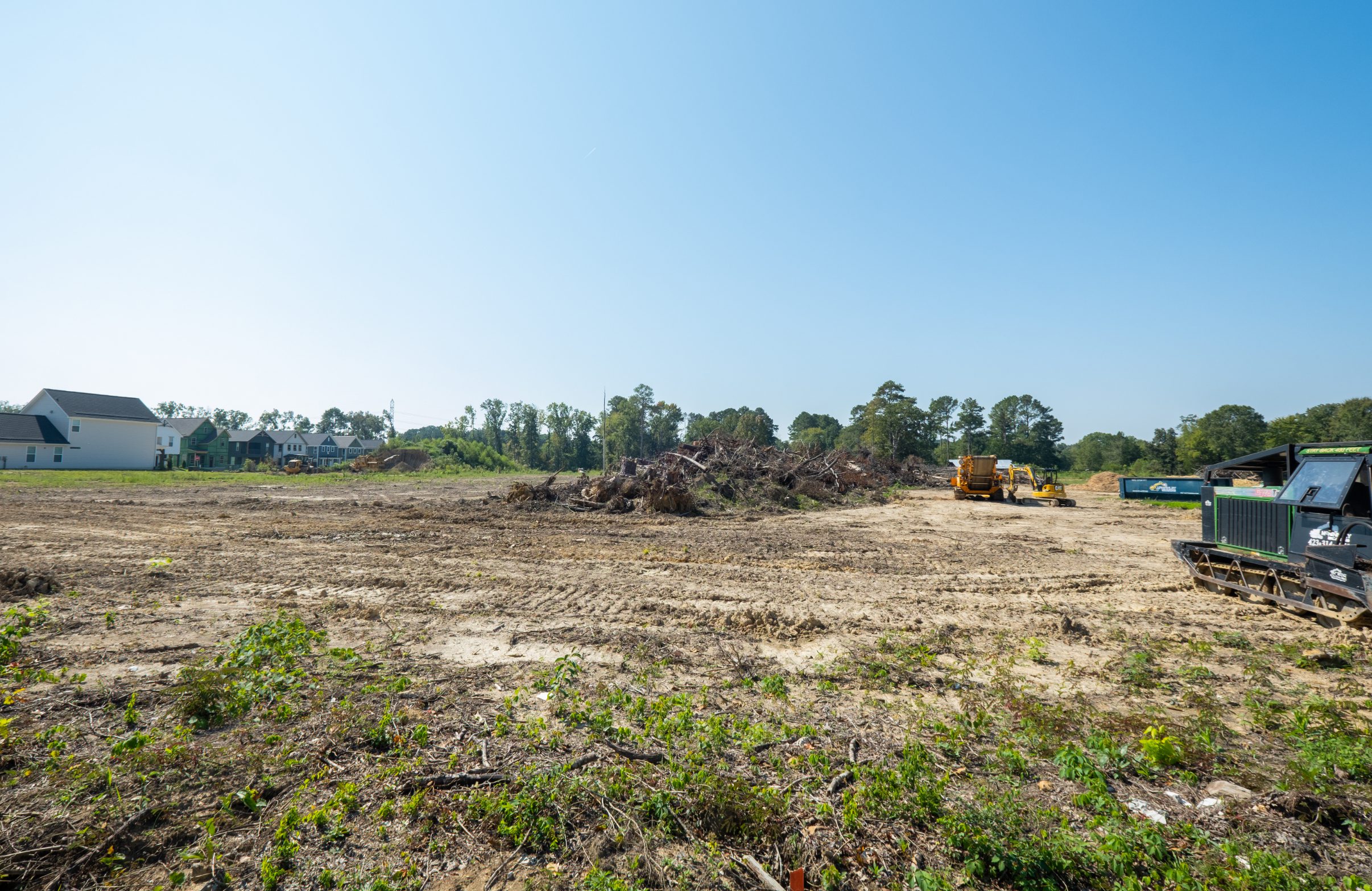 Ground-level view of the cleared site with stumps stacked and equipment working