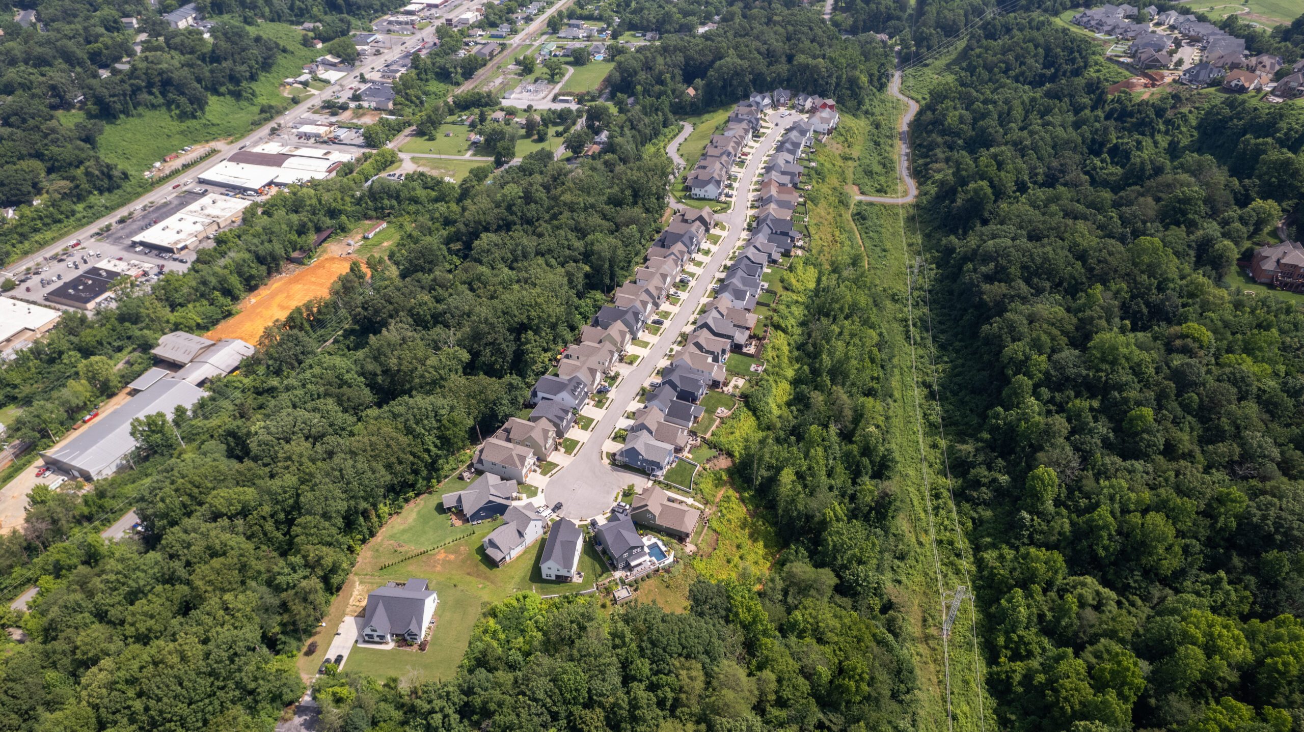 Wide aerial of Northpoint Ridge in its setting, the neighborhood running along the wooded ridge with commercial buildings and the highway below