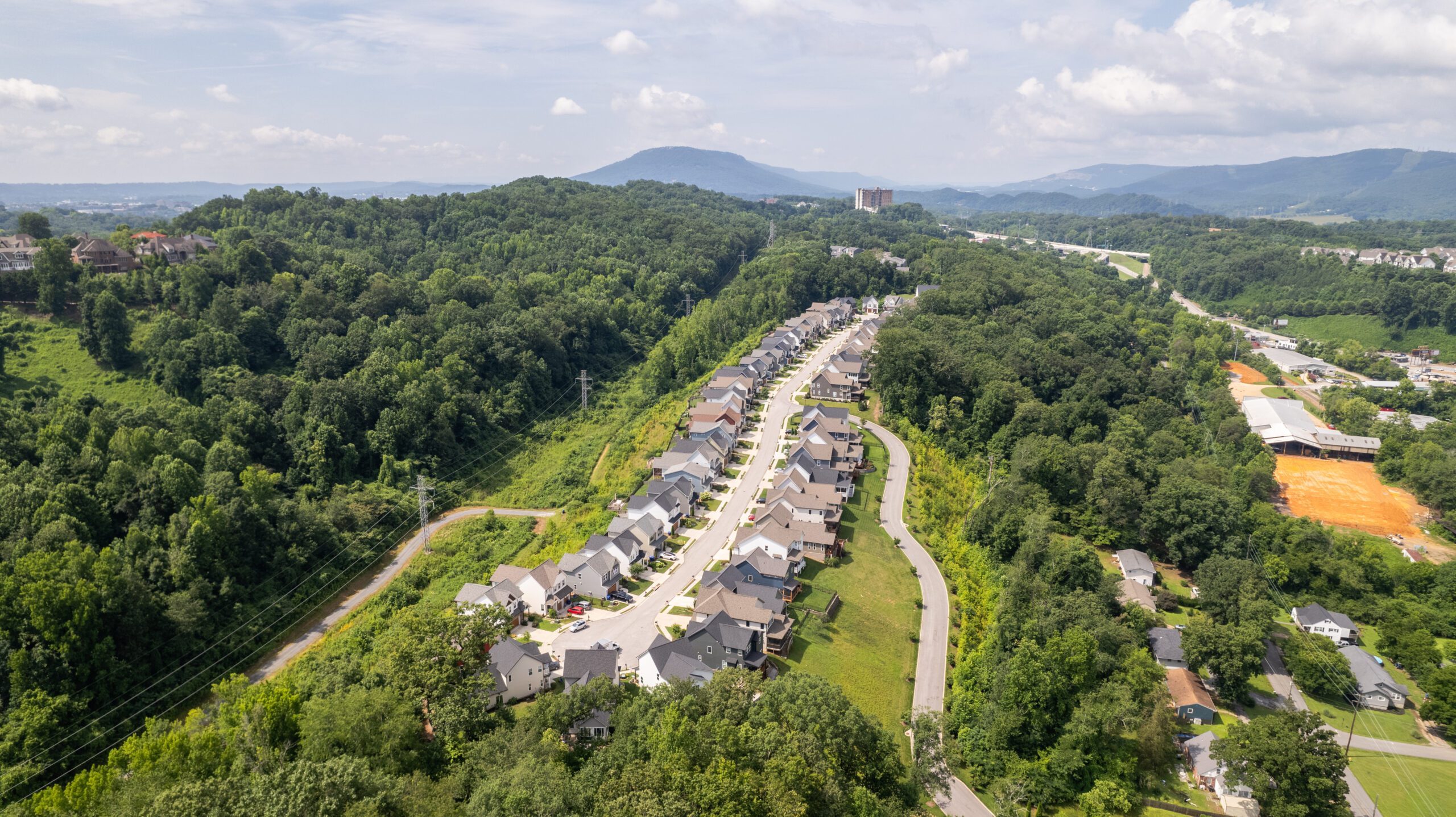 Aerial view of the Northpoint Ridge neighborhood running along a wooded ridgetop, with rows of homes on both sides of a single street and mountains beyond