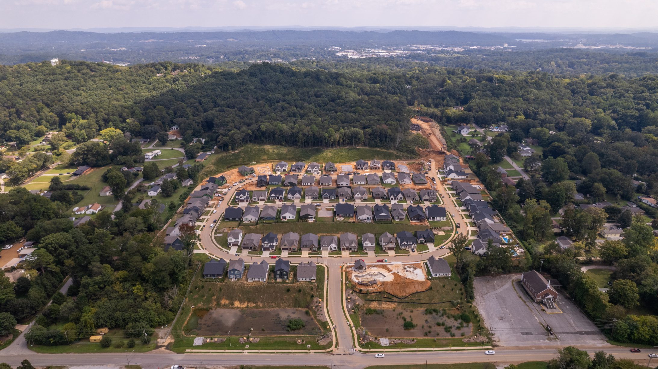 Aerial view across rows of completed homes at Painted Ridge with newer construction and the wooded ridge beyond